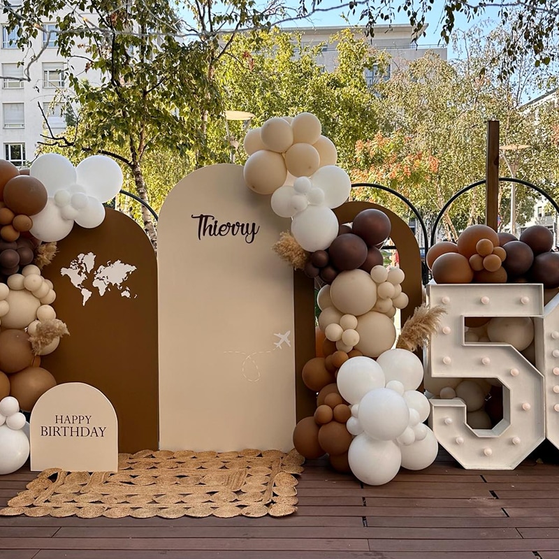 Décoration d'anniversaire thème voyage pour "Thierry" avec ballons marron, beige et blanc, carte du monde et chiffre 5 lumineux.